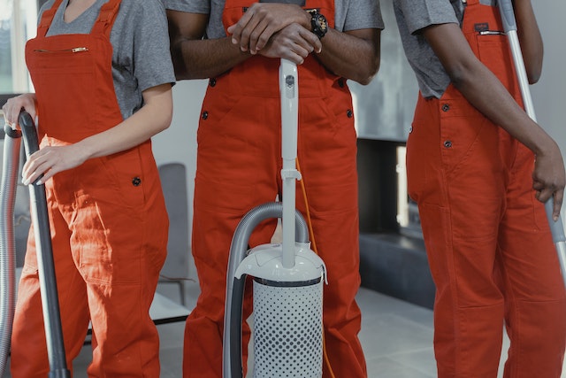 group of three professional cleaners in orange overalls holding various cleaning products